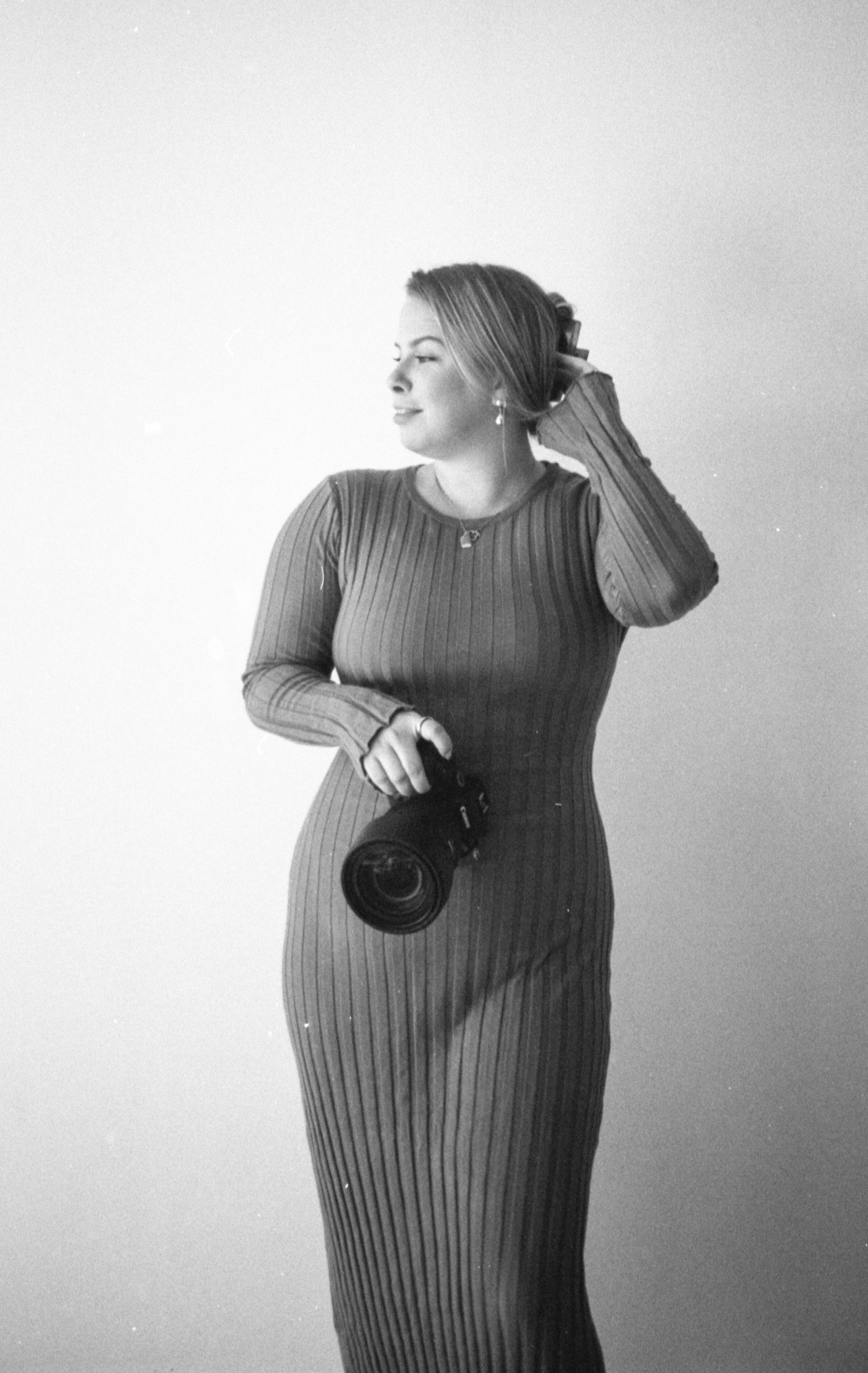 Professional portrait of a woman in a fitted ribbed dress holding camera equipment in black and white.