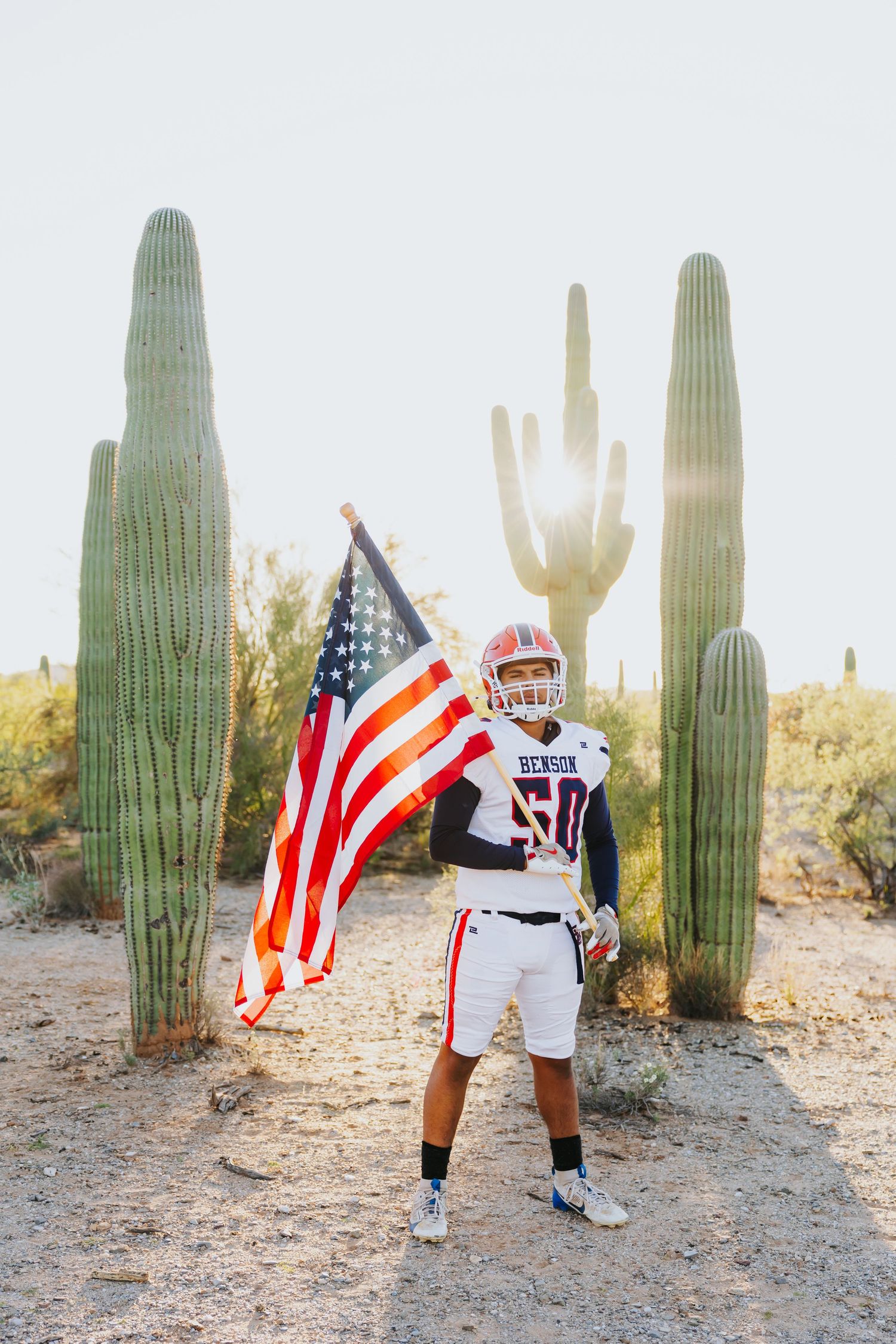 Person holding an American flag poses near tall saguaro cacti in the Arizona desert.