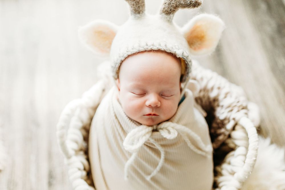 A sleeping infant wrapped in soft white fabric lies peacefully on a textured white blanket.