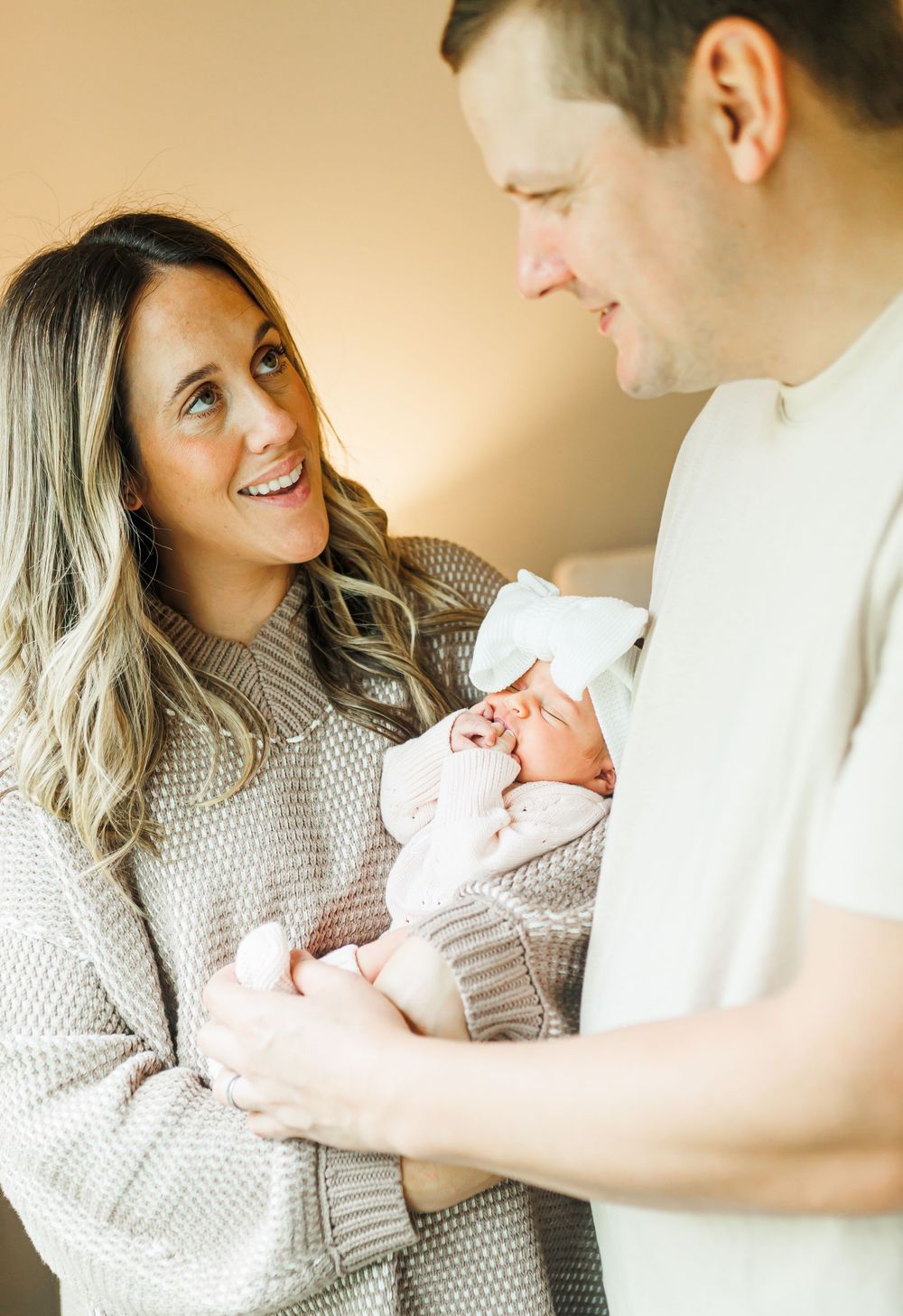 A tender family moment captured in warm tones as parents gaze lovingly at their newborn baby in a cozy home setting.