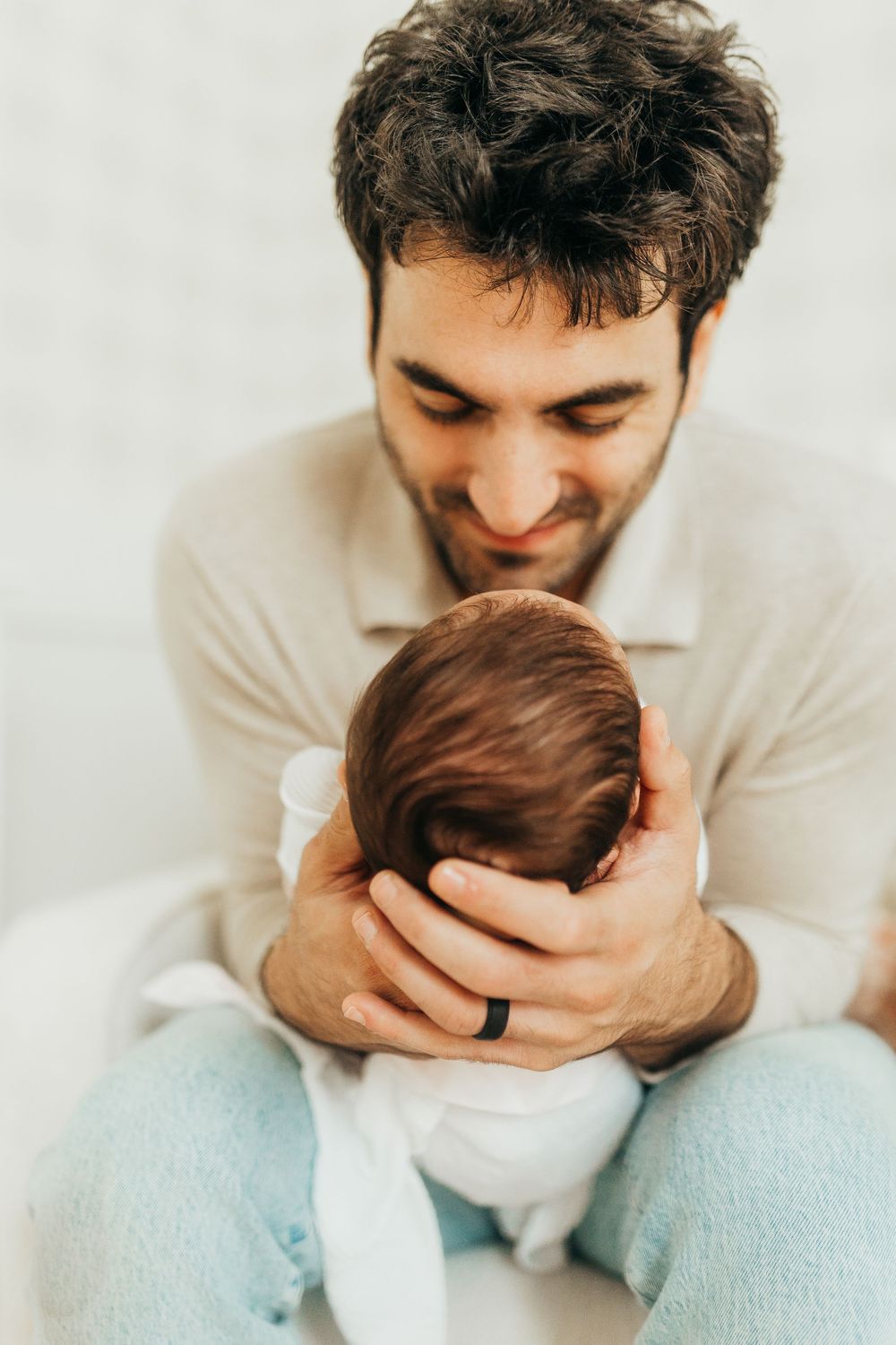 A parent lovingly cradles and gazes at their newborn baby while wearing a cream colored sweater.