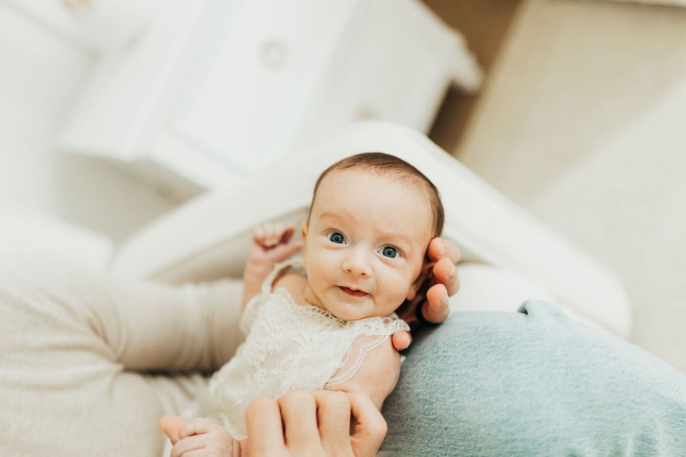 A tender moment between parent and baby lying on white bedding in natural light.