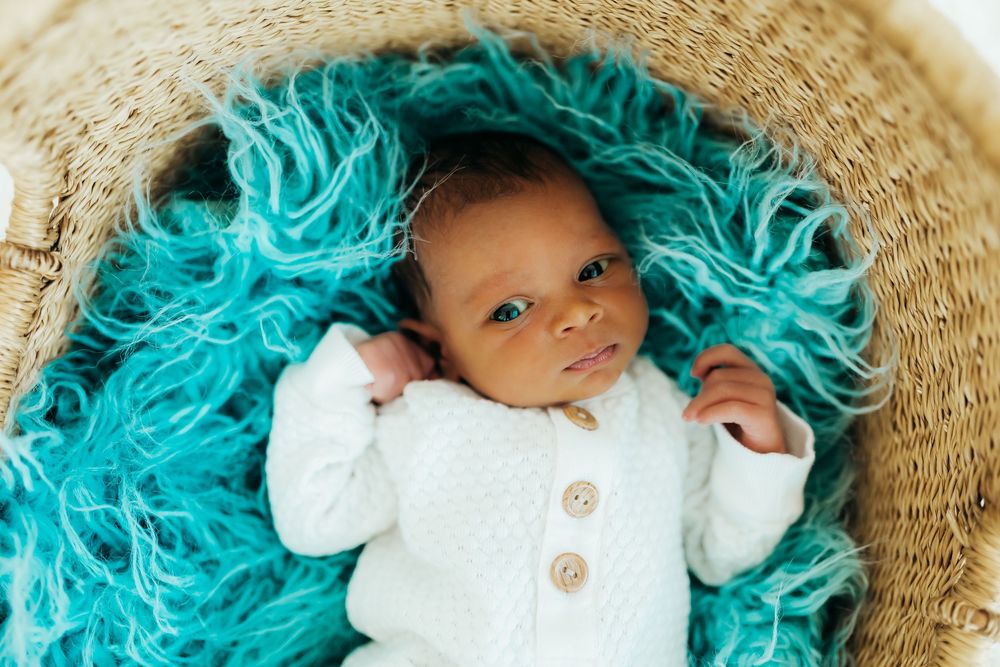 Infant wearing white sweater lying in basket with bright turquoise blue yarn or fabric.
