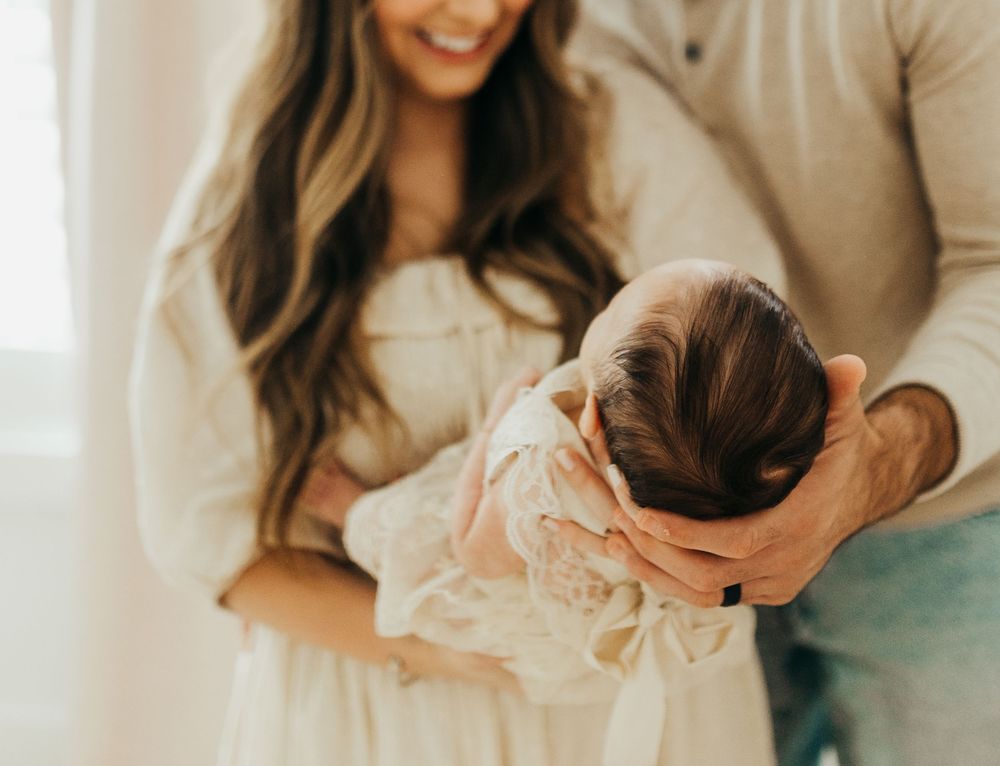 A newborn baby wearing white lace is gently cradled in loving arms during an intimate family photo session.