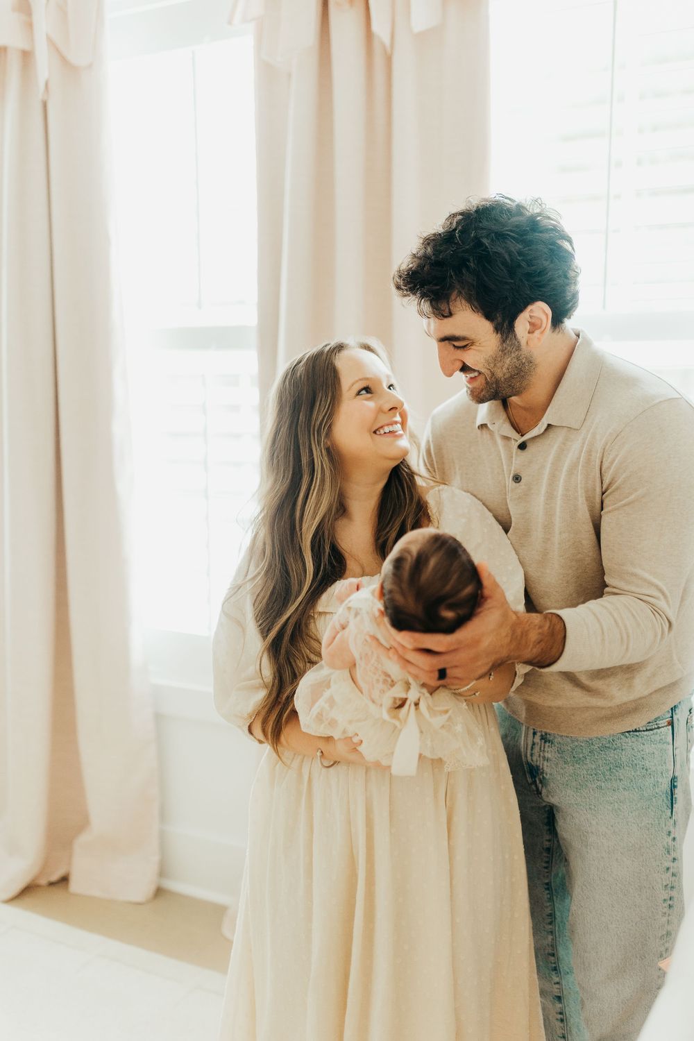 A couple shares joyful moments with their newborn baby in a bright, sunlit room.