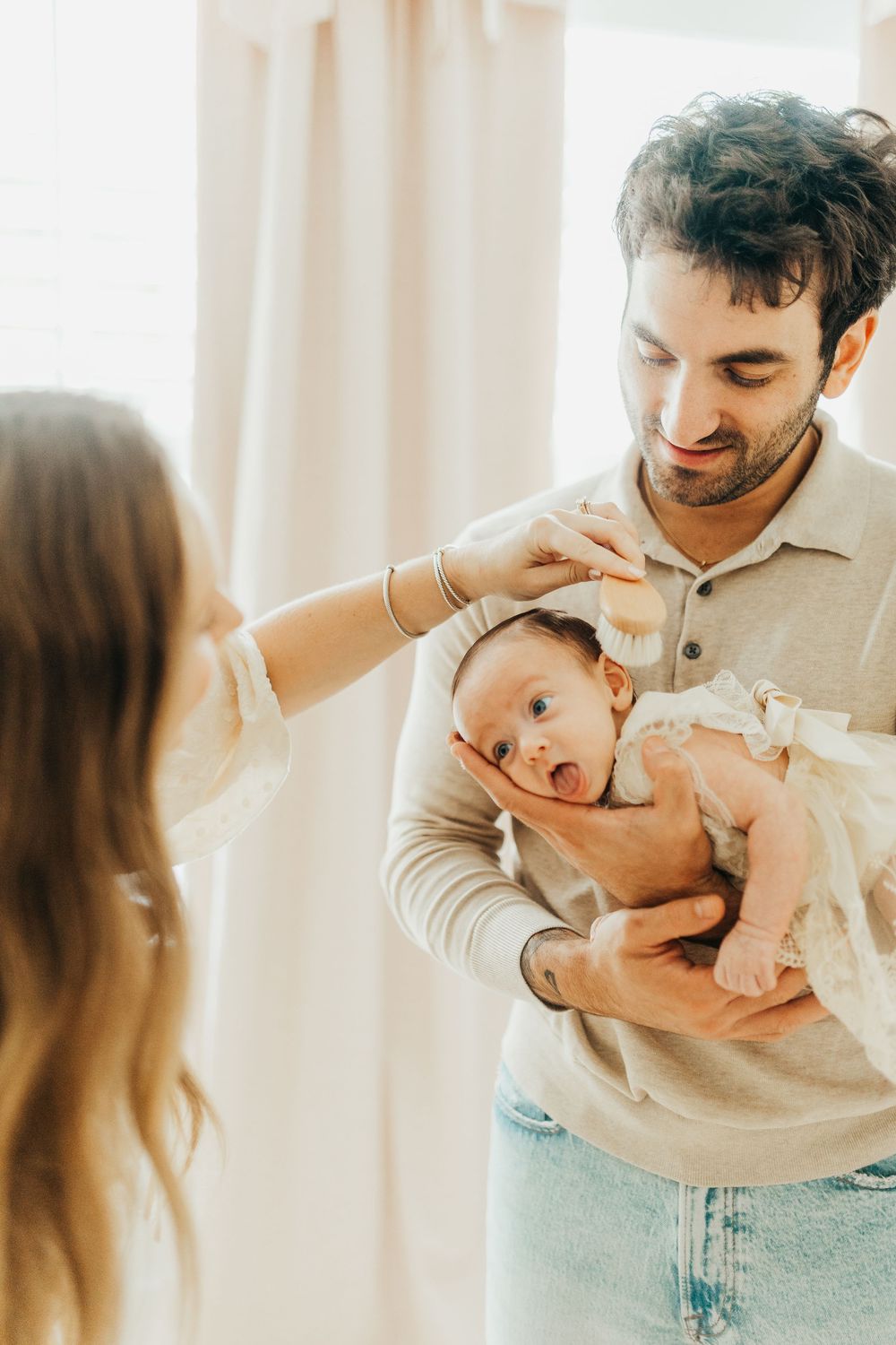 Parents share tender moments with their yawning newborn baby in natural window light.