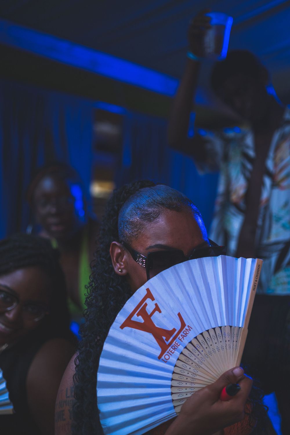 Person holding a white folding fan illuminated by blue nightclub lighting creating a moody party atmosphere.