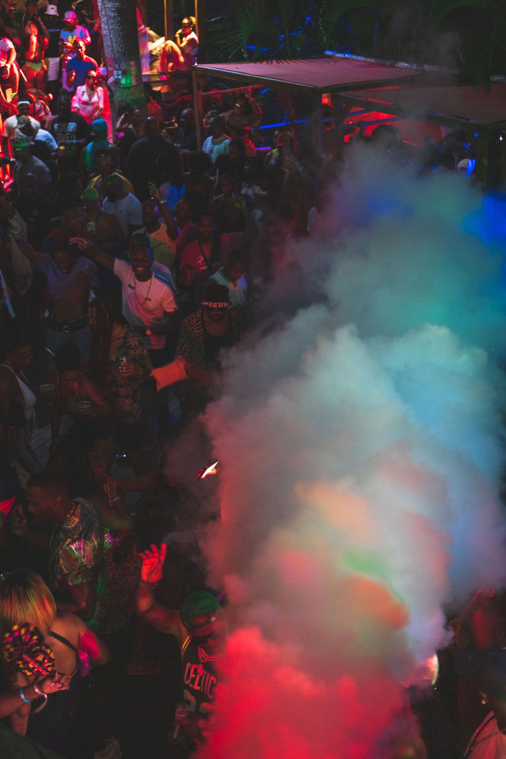 Crowded nightclub dance floor with atmospheric smoke effects and colorful red and blue lighting during a party.