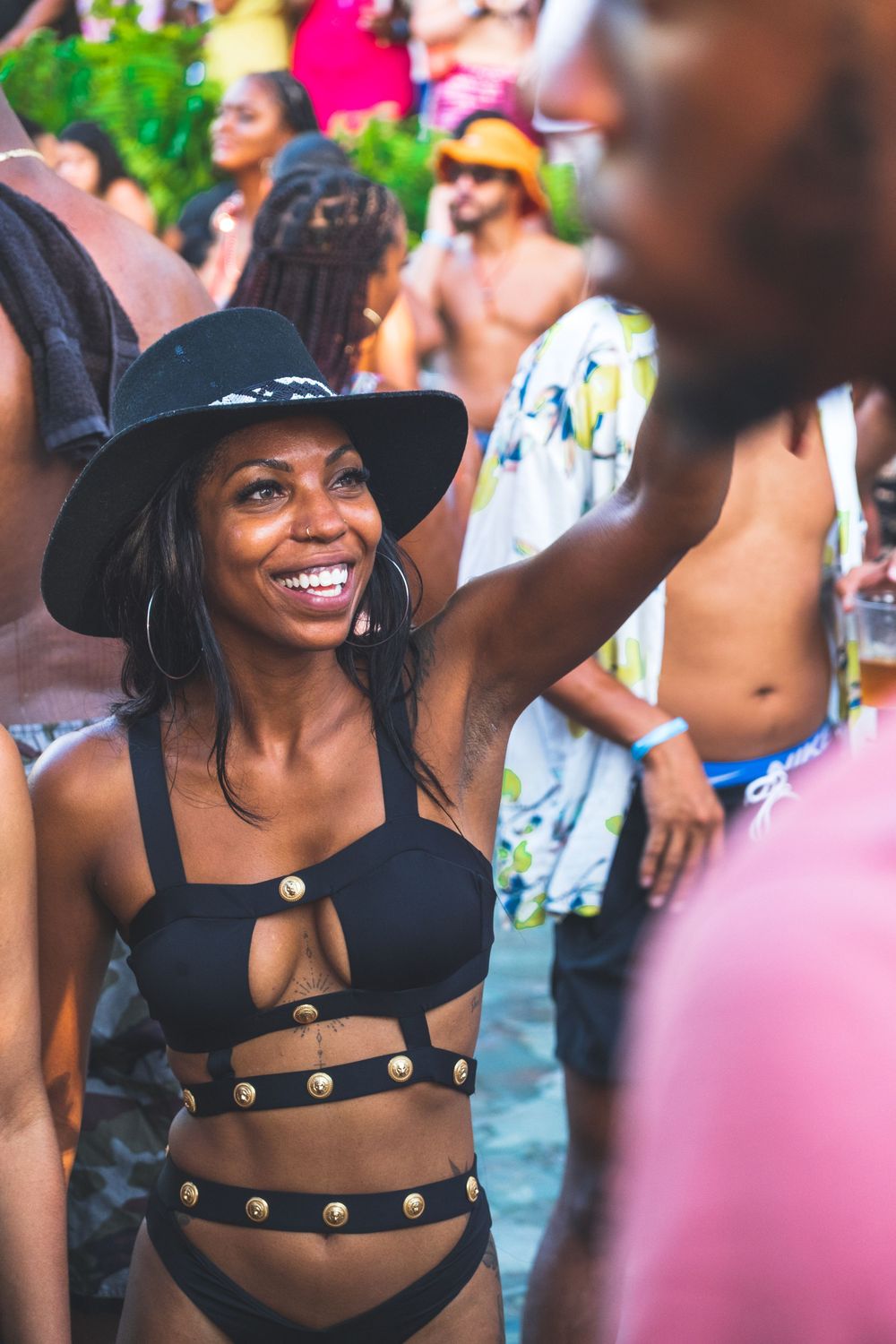 Festival goer dances and smiles while wearing a black hat and cutout swimsuit at an outdoor summer event.