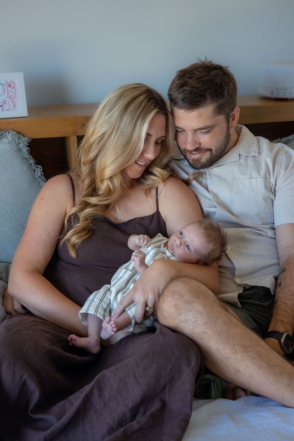 A couple cuddles with their sleeping newborn baby while relaxing together on a couch at home.