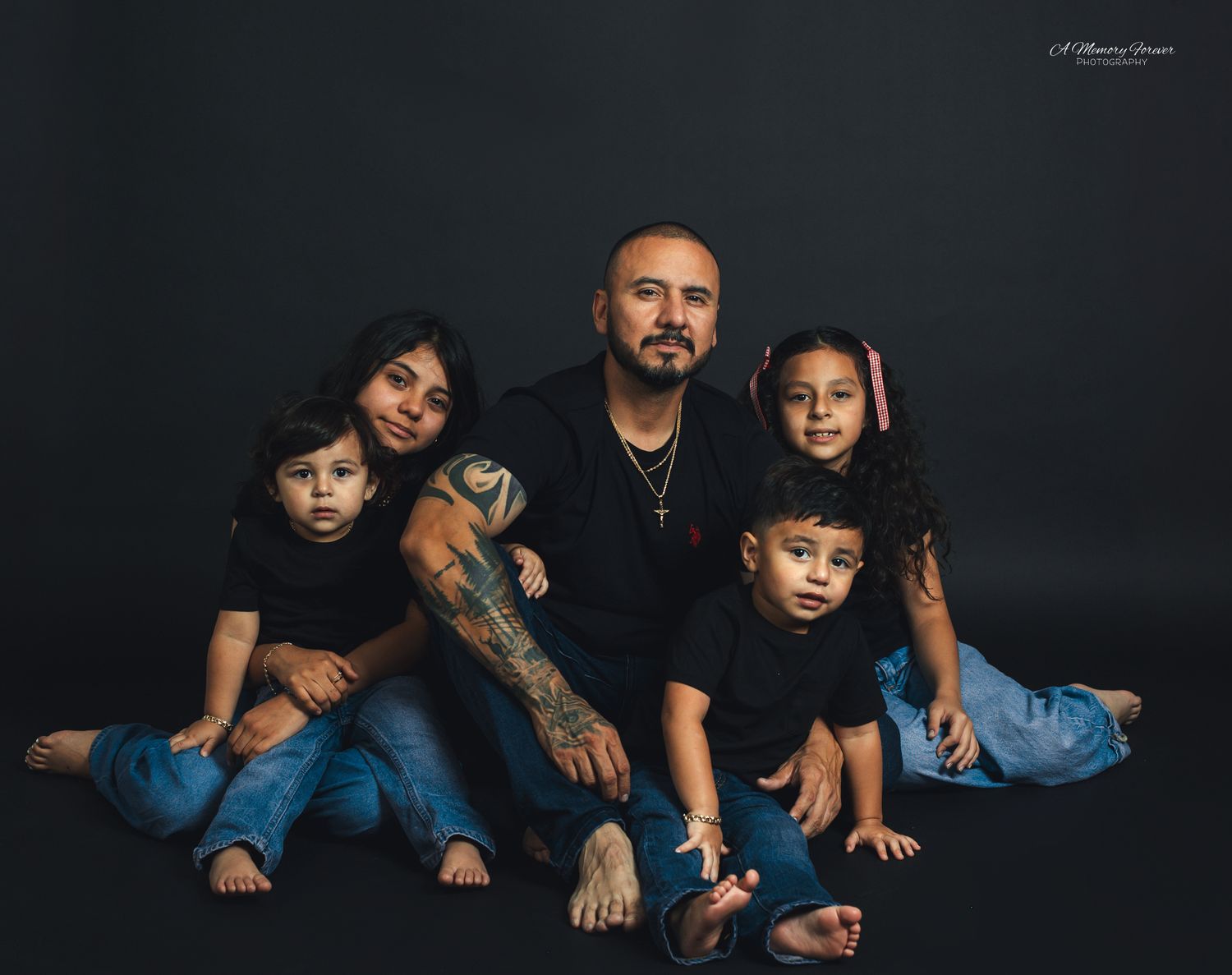 Family of five posing together in matching black outfits against a dark studio background for a professional portrait.
