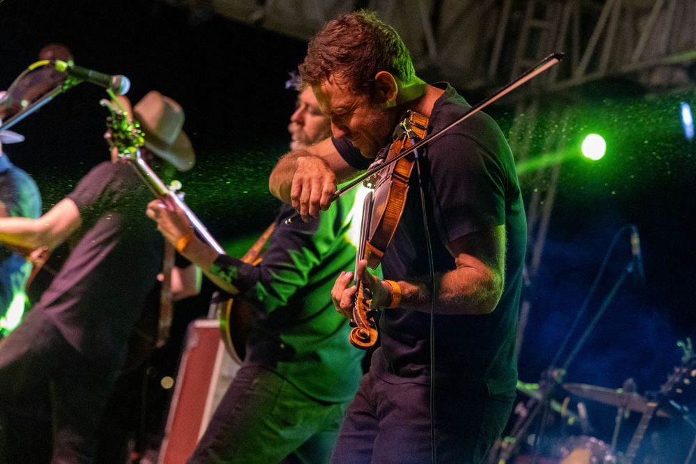 Violinist performs passionately on stage illuminated by green lighting during a concert.