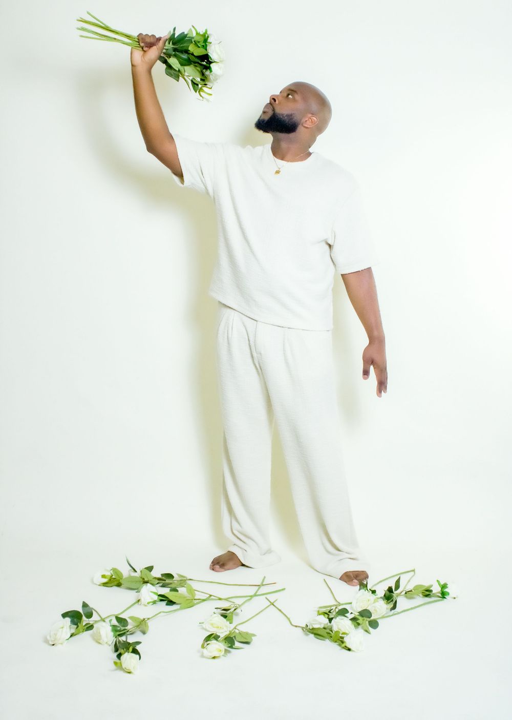 Person in white outfit holding fresh herbs against white background with greenery.
