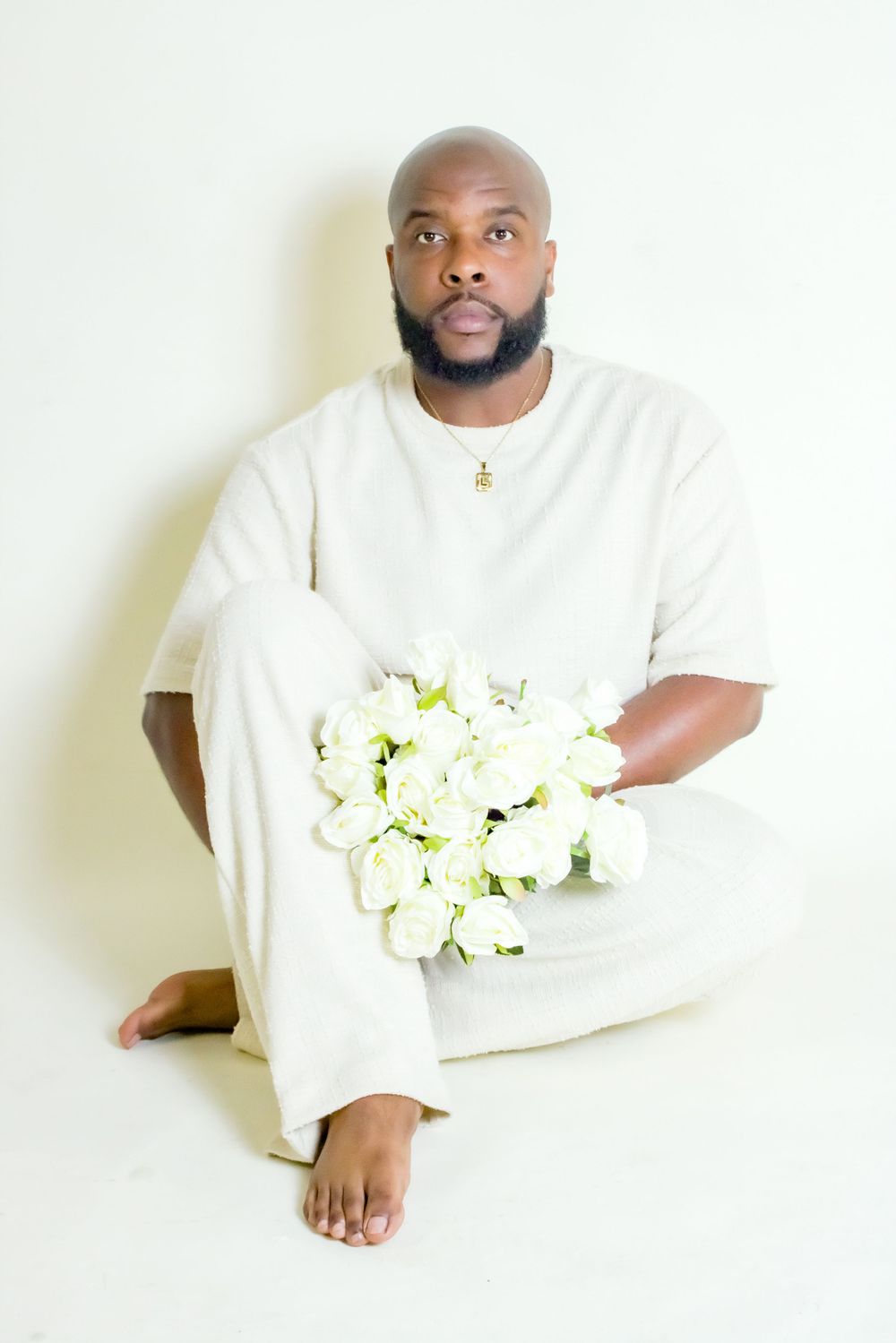 Person in white clothing holding bouquet of white flowers against minimalist background.