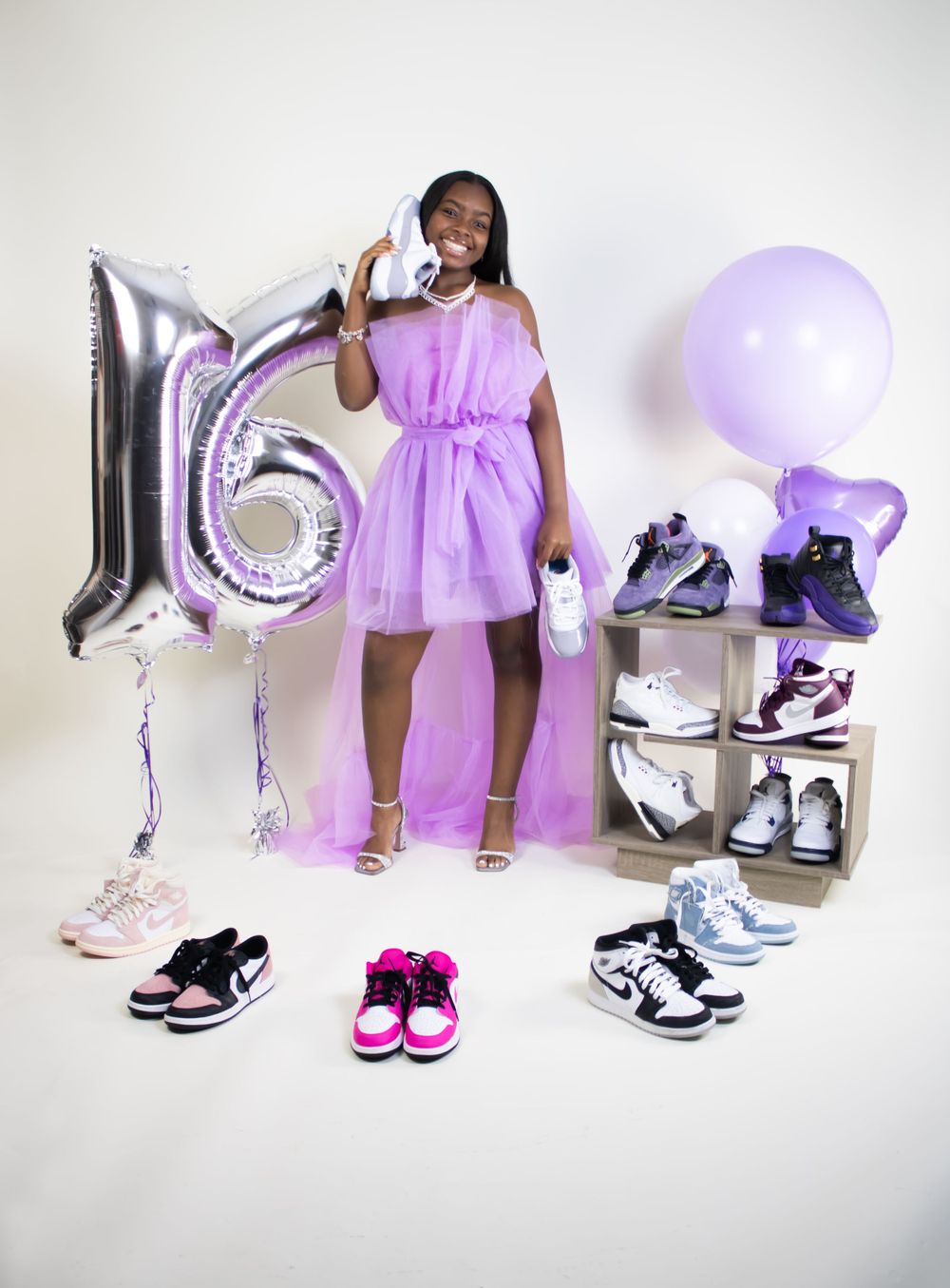 Person in purple dress displaying sneaker collection with number 16 balloon decoration.