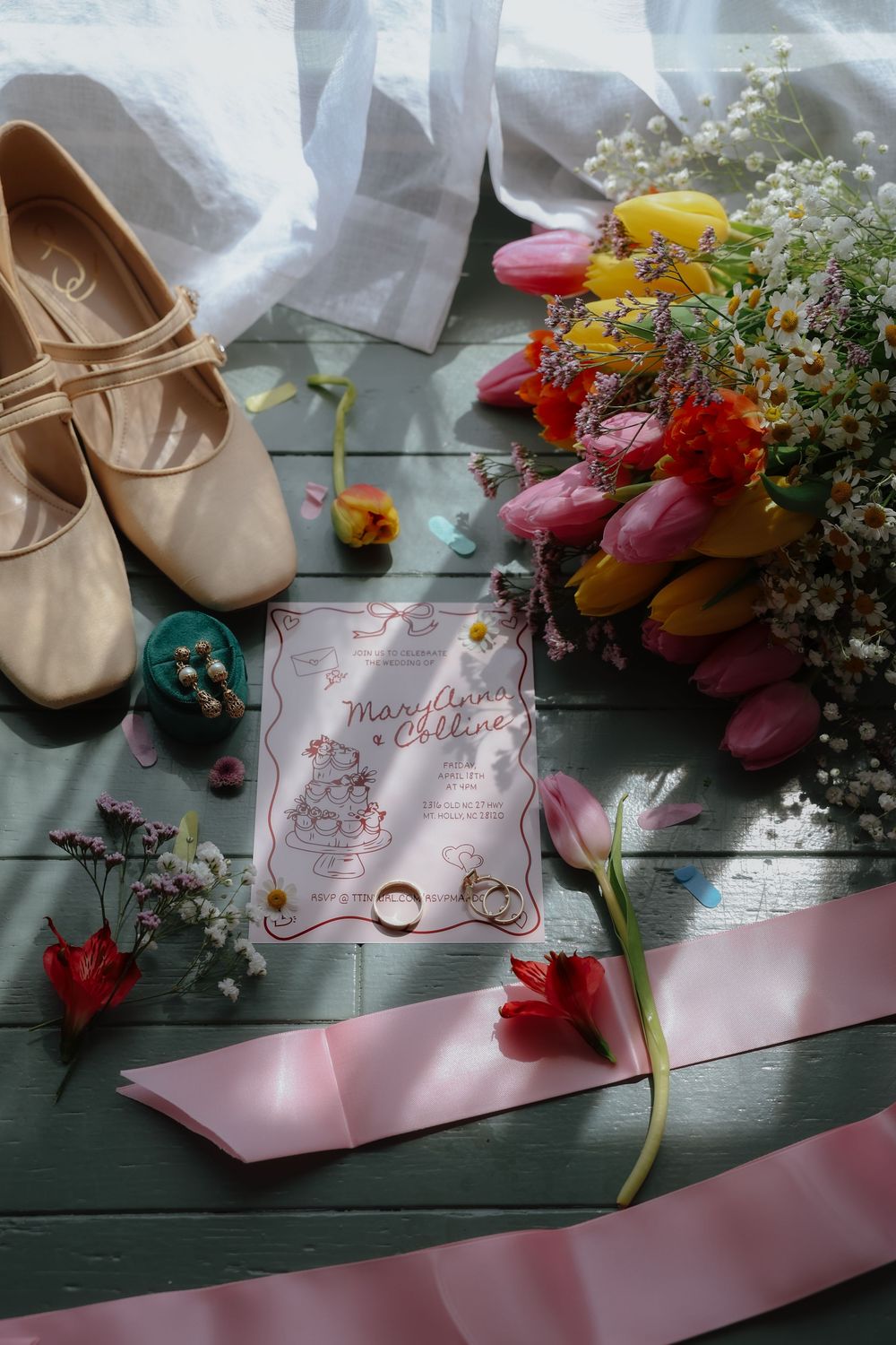 Ballet shoes, floral arrangements and wedding invitations arranged on a dark green wooden surface.