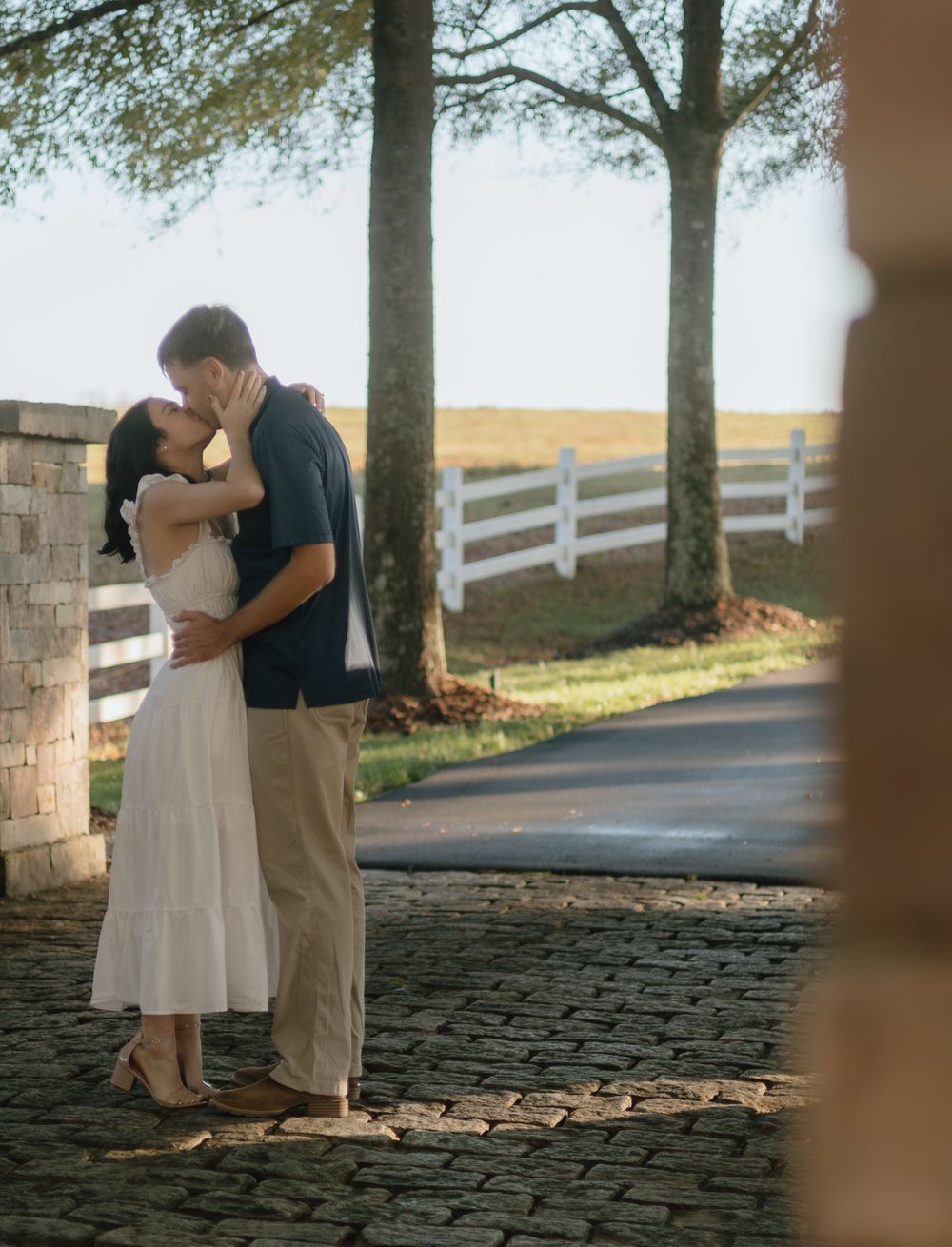 A romantic moment shared on a cobblestone path with white fencing in the background.