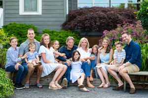 Large family group portrait outdoors on steps of grey house with landscaping.