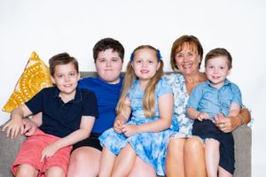 Grandmom and grandchildren sitting close together on couch with gold pillow against white background.