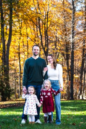 A family poses together in a vibrant autumn forest setting with golden leaves and green grass.