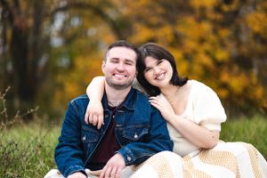Couple in casual attire sitting together on grassy hill during autumn.