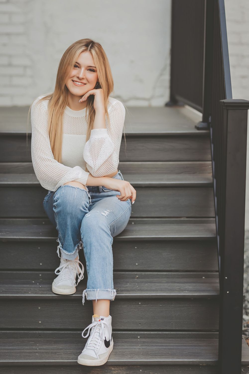 Casual style photoshoot on gray concrete steps featuring light jeans, white sweater and white sneakers.