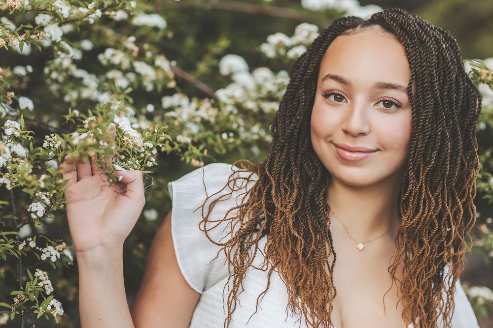 Woman with curly hair poses outdoors among white flowering bushes in springtime.