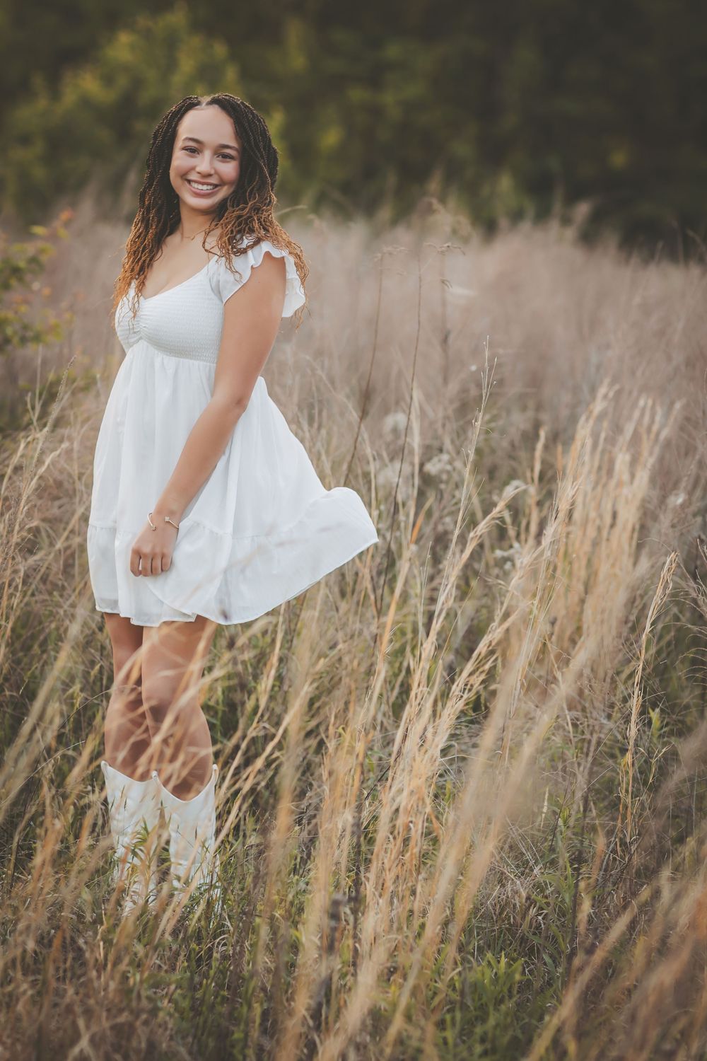 Ethereal portrait in a flowing white dress against tall prairie grass at sunset.