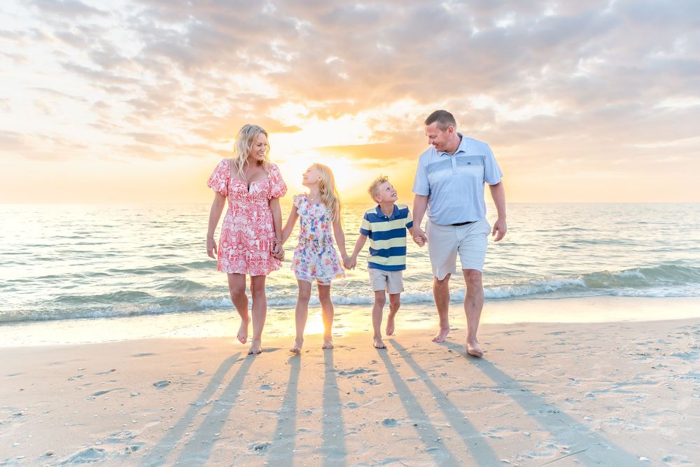 A family walks along the beach at sunset holding hands with their backs to the camera.