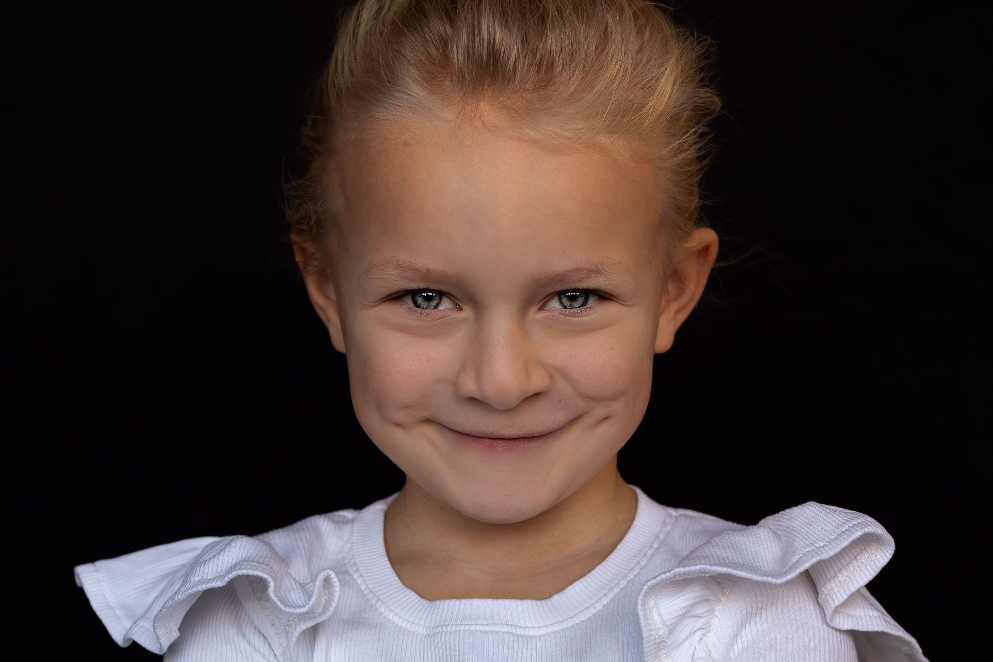 Barbara Kempeneers Fotografie, Kinderportret, Zwarte achtergrond, Meisje met ontdeugende lach