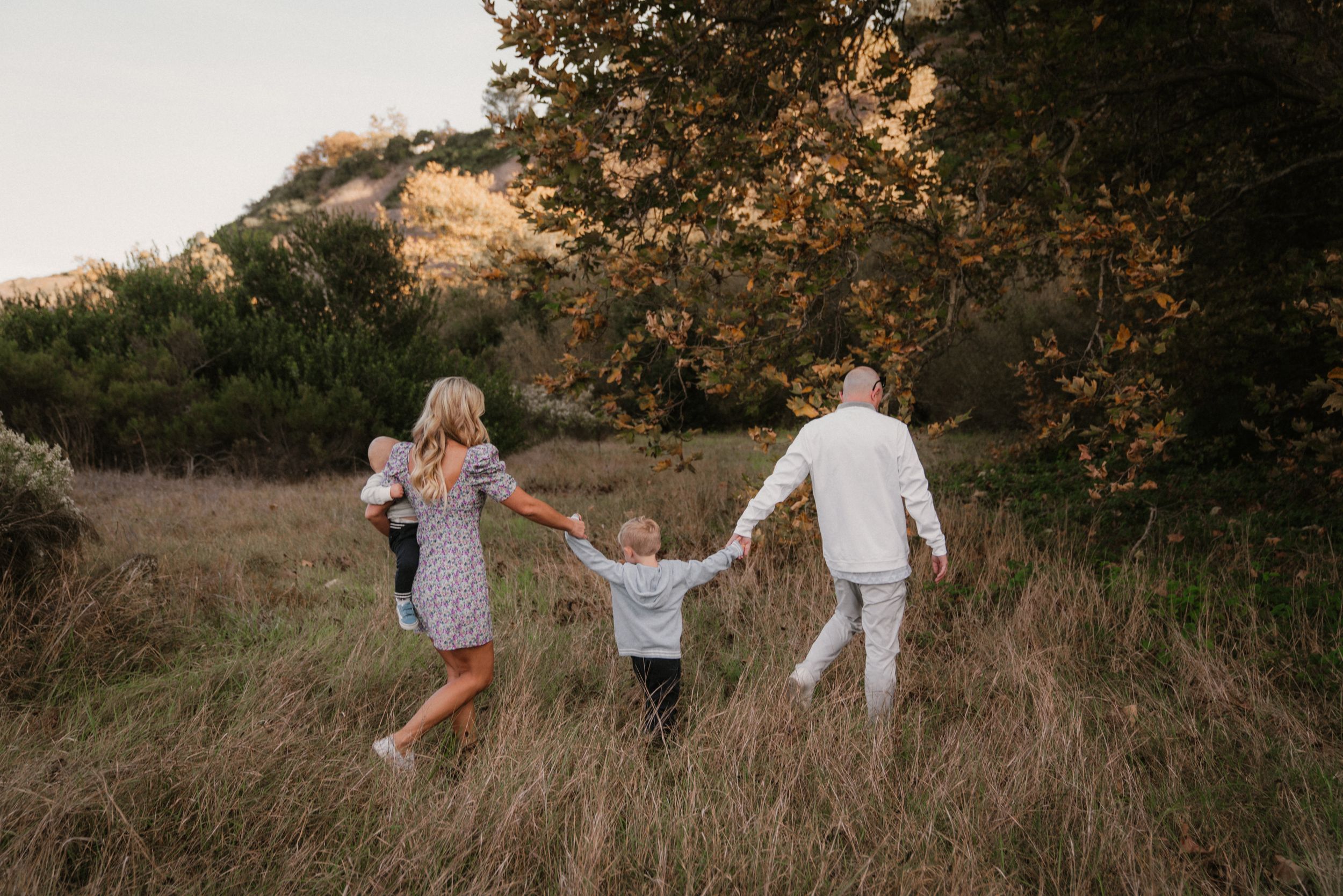 A family holds hands while walking through a golden field at sunset.
