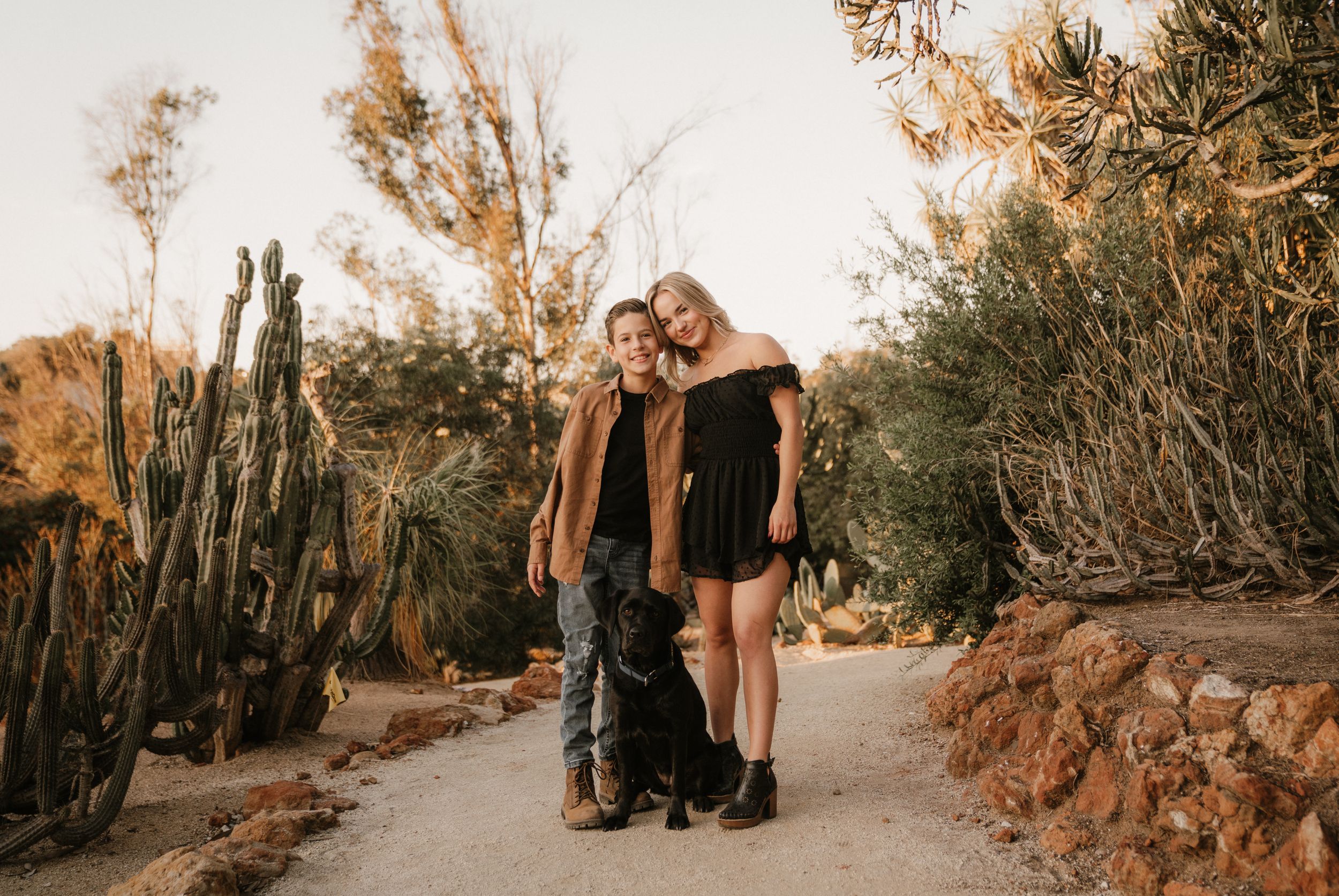 A group poses together on a desert trail surrounded by tall cacti and natural landscaping.