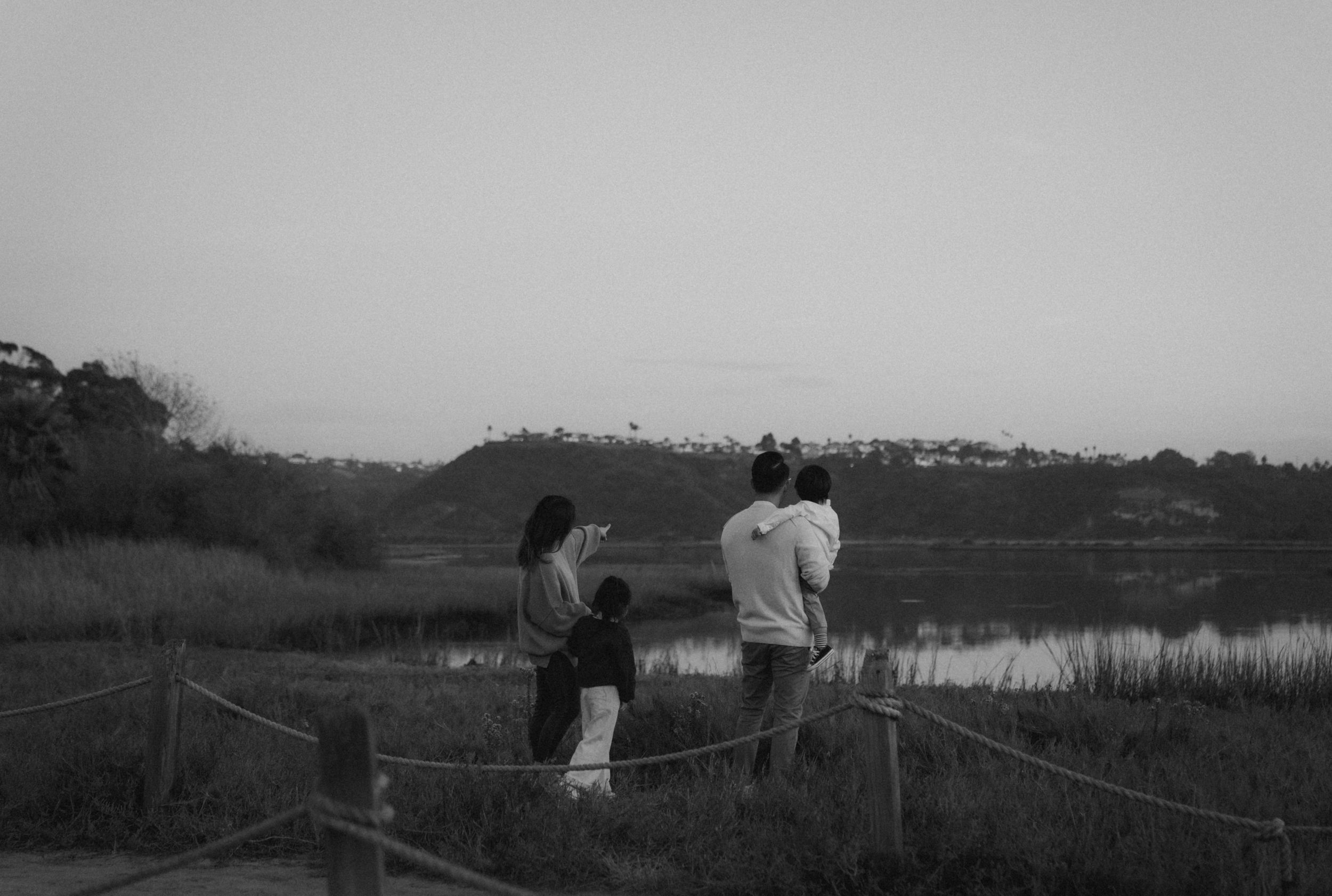 Two figures sit together on a wooden fence overlooking a serene lake at twilight.