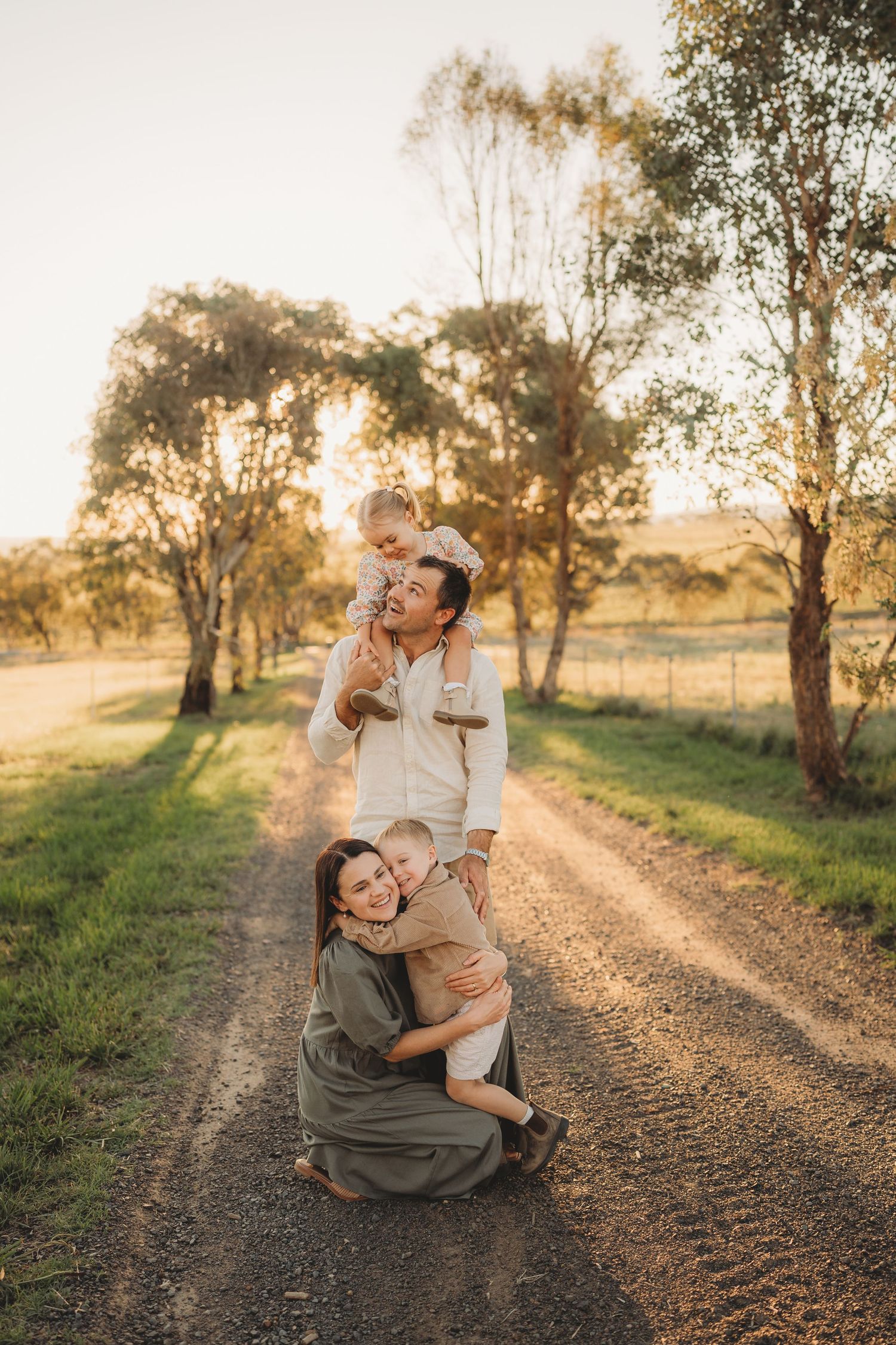 Family portrait on a dirt road at golden hour with parents and two young children.
