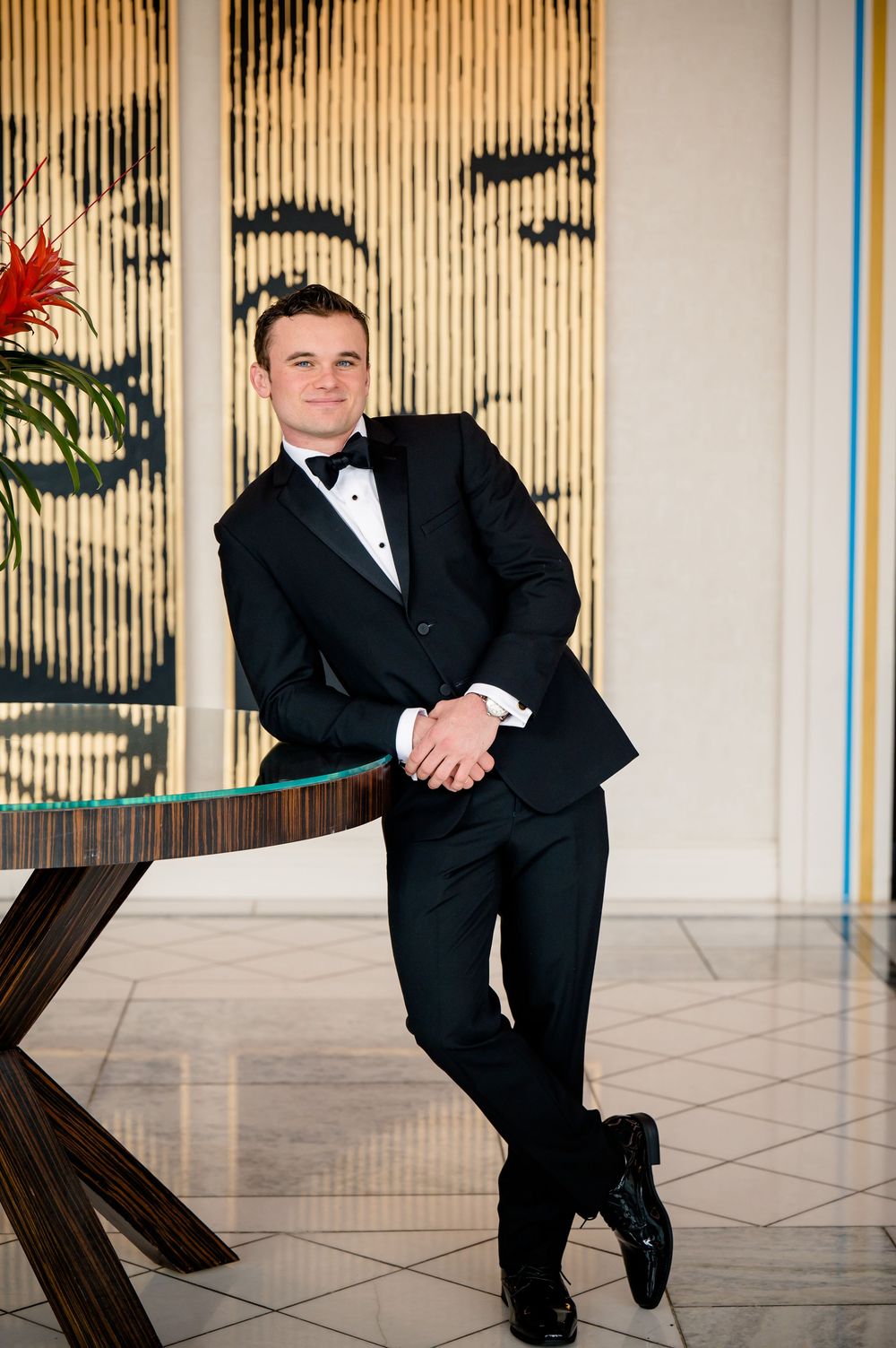 A man wearing black formal attire leans on a wall in four similar poses at an indoor venue.