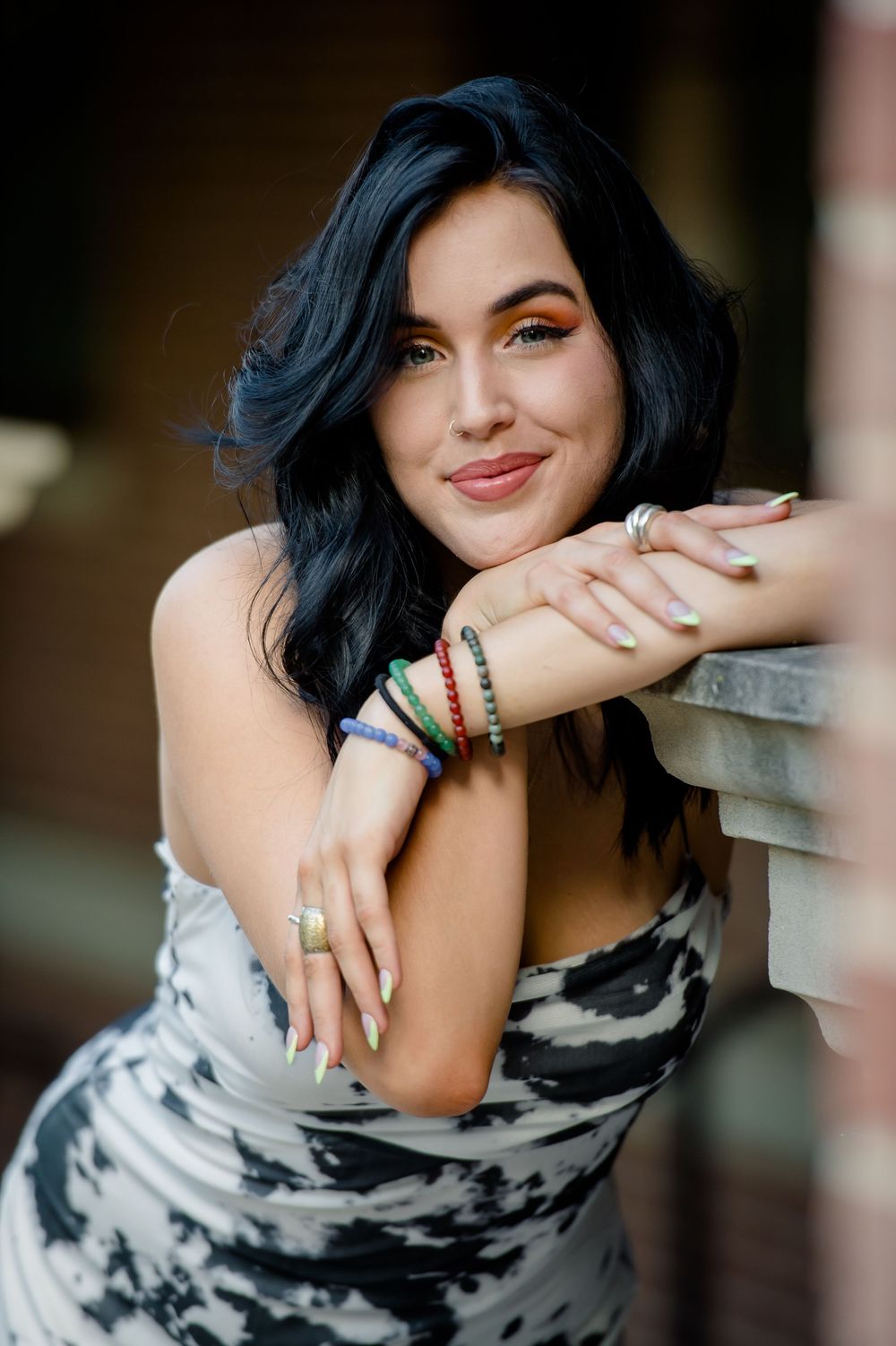Woman with dark wavy hair wearing black and white tie-dye dress poses with colorful bracelets and rings.