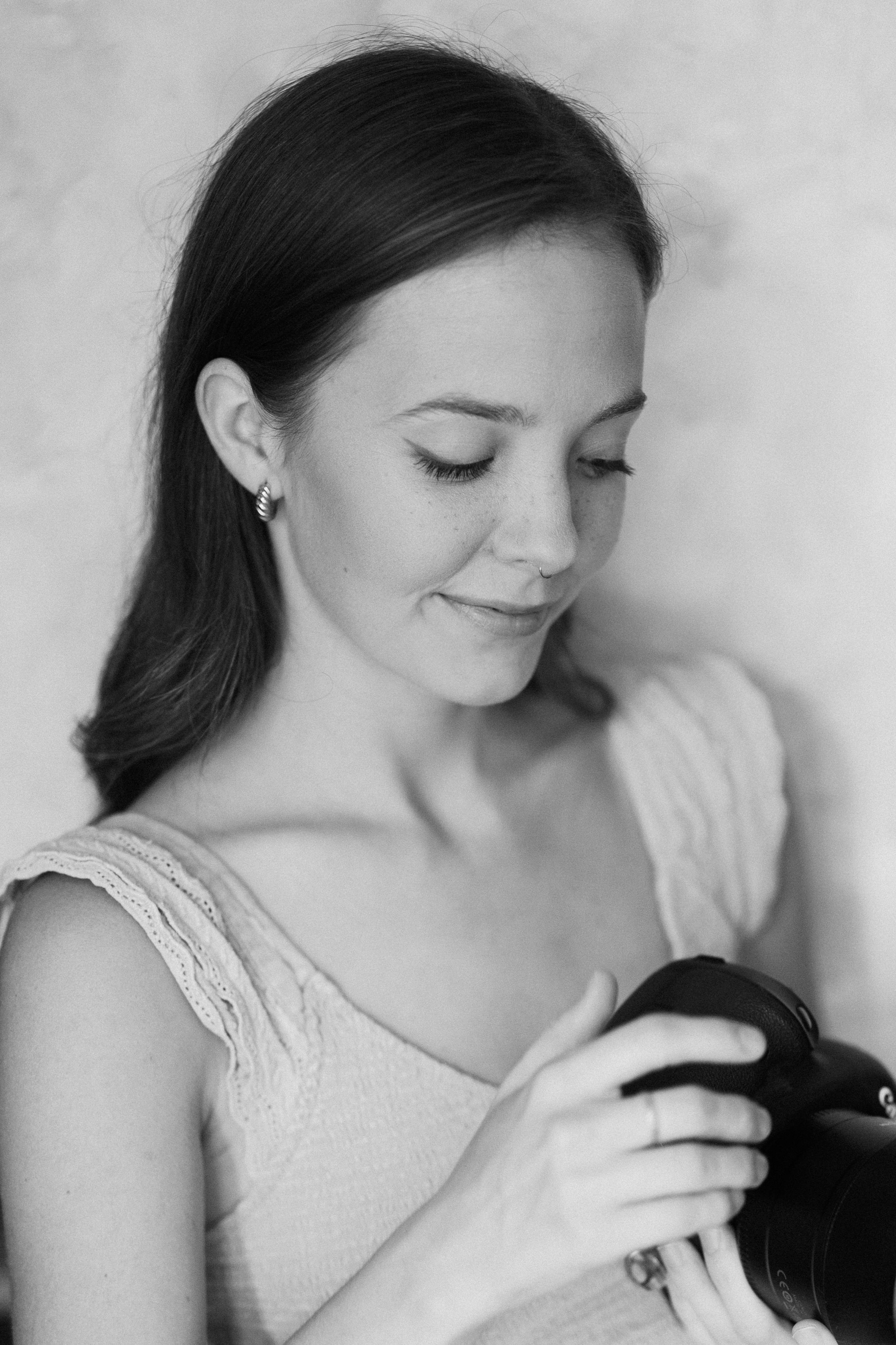 Studio portrait of a woman with dark hair in a light-colored top looking down with closed eyes.