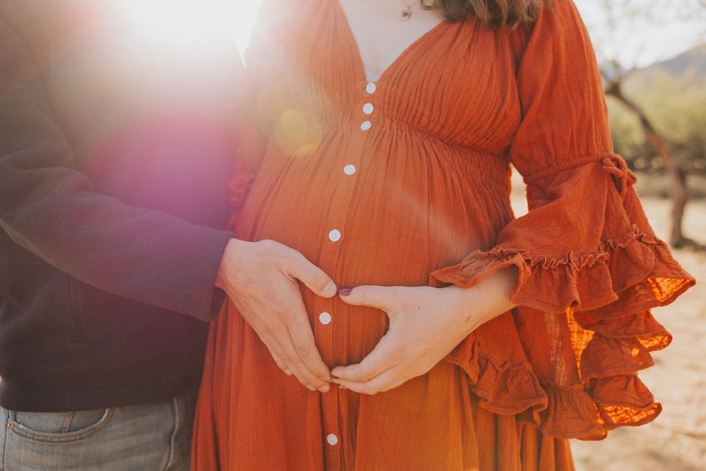 A close-up shot of a maternity dress in bright rust orange with ruffled sleeves and button details.