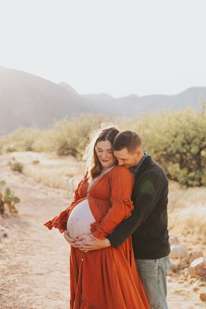 An intimate maternity photoshoot in a desert landscape with warm lighting.