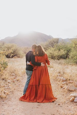 Women in matching red dresses pose together in desert landscape at sunset.