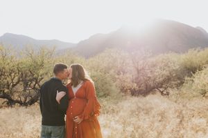 Intimate desert maternity session with couple embracing against mountain backdrop.