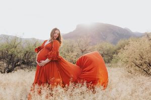 Woman in flowing red dress twirls in desert setting during maternity photoshoot.