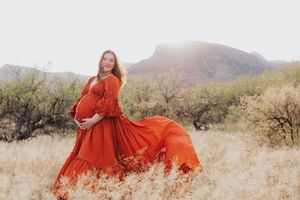 Dramatic maternity photos with red dress flowing in desert wind against mountains.