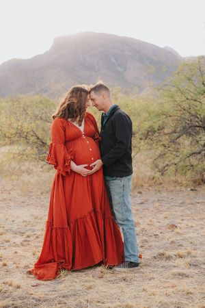 Couple shares tender moment during desert maternity photoshoot at sunset.