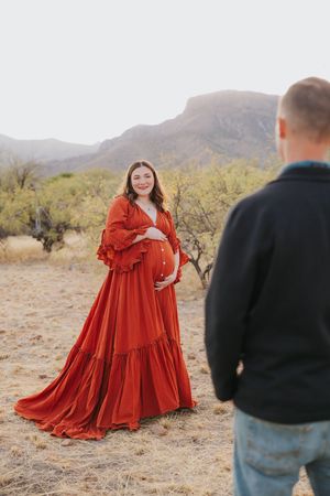 Woman in red ruffled dress poses during desert maternity photoshoot.