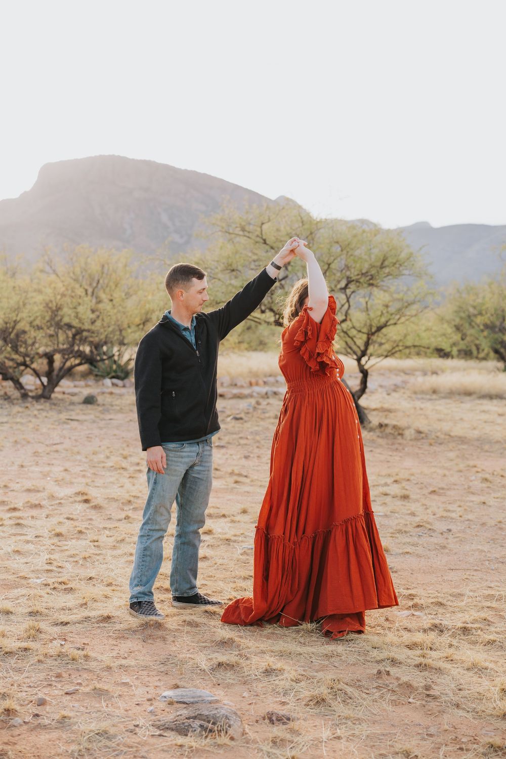 A couple dancing in a desert landscape with mountains, the woman wearing a flowing red dress.