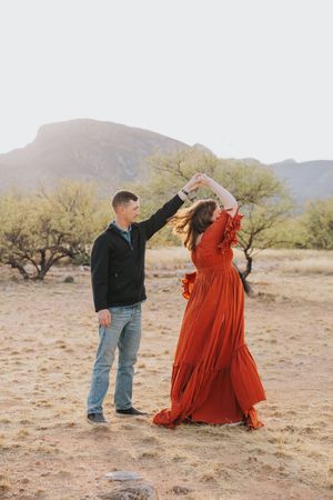 A playful dance moment captured in the desert with a flowing red dress against mountain backdrop.