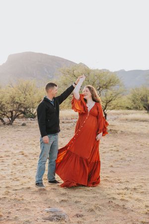 Dancing couple in desert setting with mountains, featuring dramatic red maxi dress and casual attire.