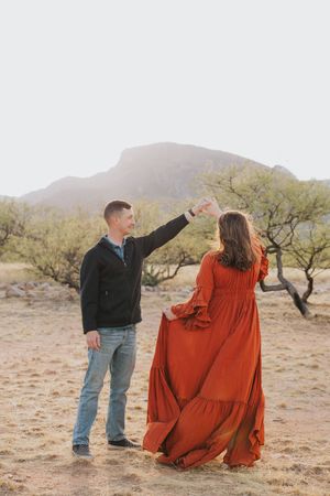Couple dancing together on desert path with mountains and desert vegetation in background.