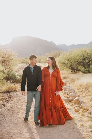 Couple strolling along desert path with mountain backdrop and desert vegetation.